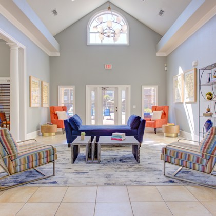 Long view of the apartment community clubhouse with multiple seating areas, grey walls, and windows letting in natural light